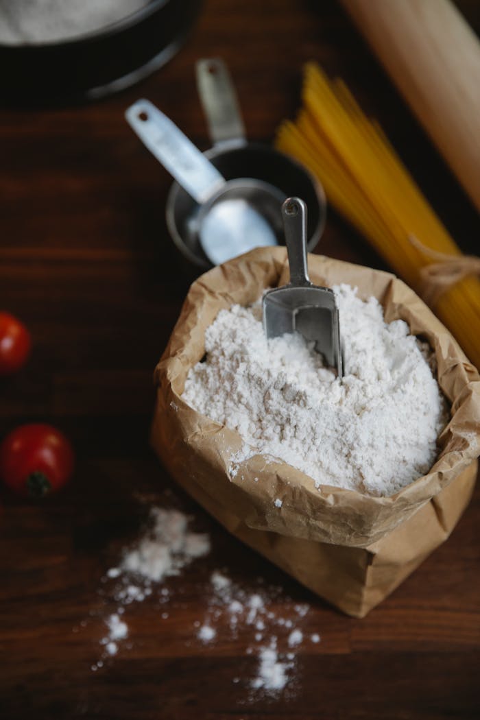 High angle of wheat flour in paper bag placed with tomatoes and raw spaghetti for recipe